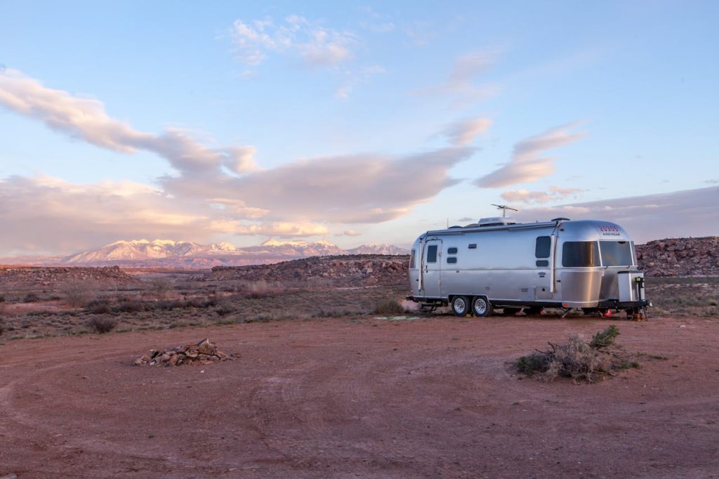 Home Silver trailer in desert landscape at sunset with mountains in the background.