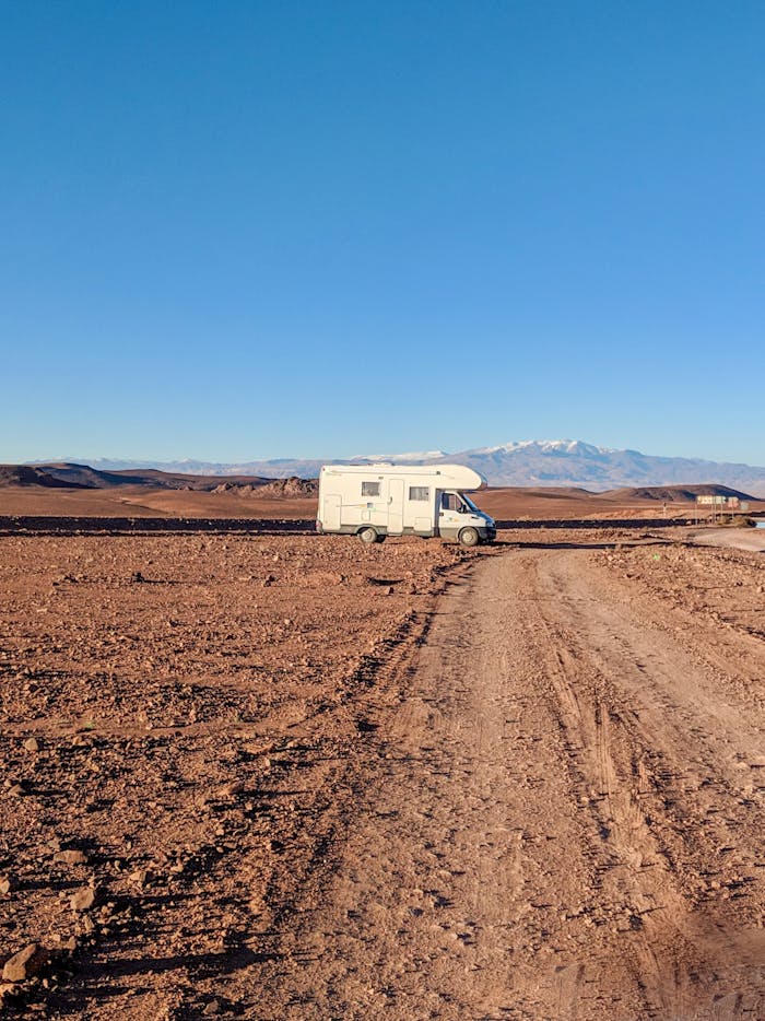 Home Campervan travels through arid desert landscape under clear blue sky in Morocco.